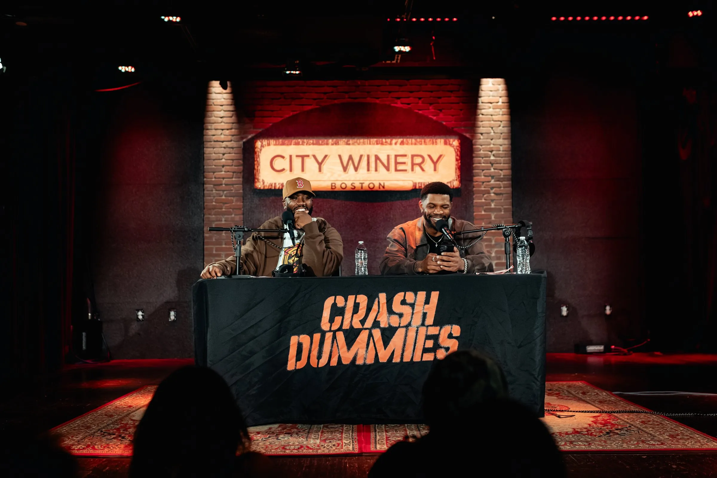 Mike and Pat on stage at City Winery Boston behind the Crash Dummies table, with the crowd in the foreground