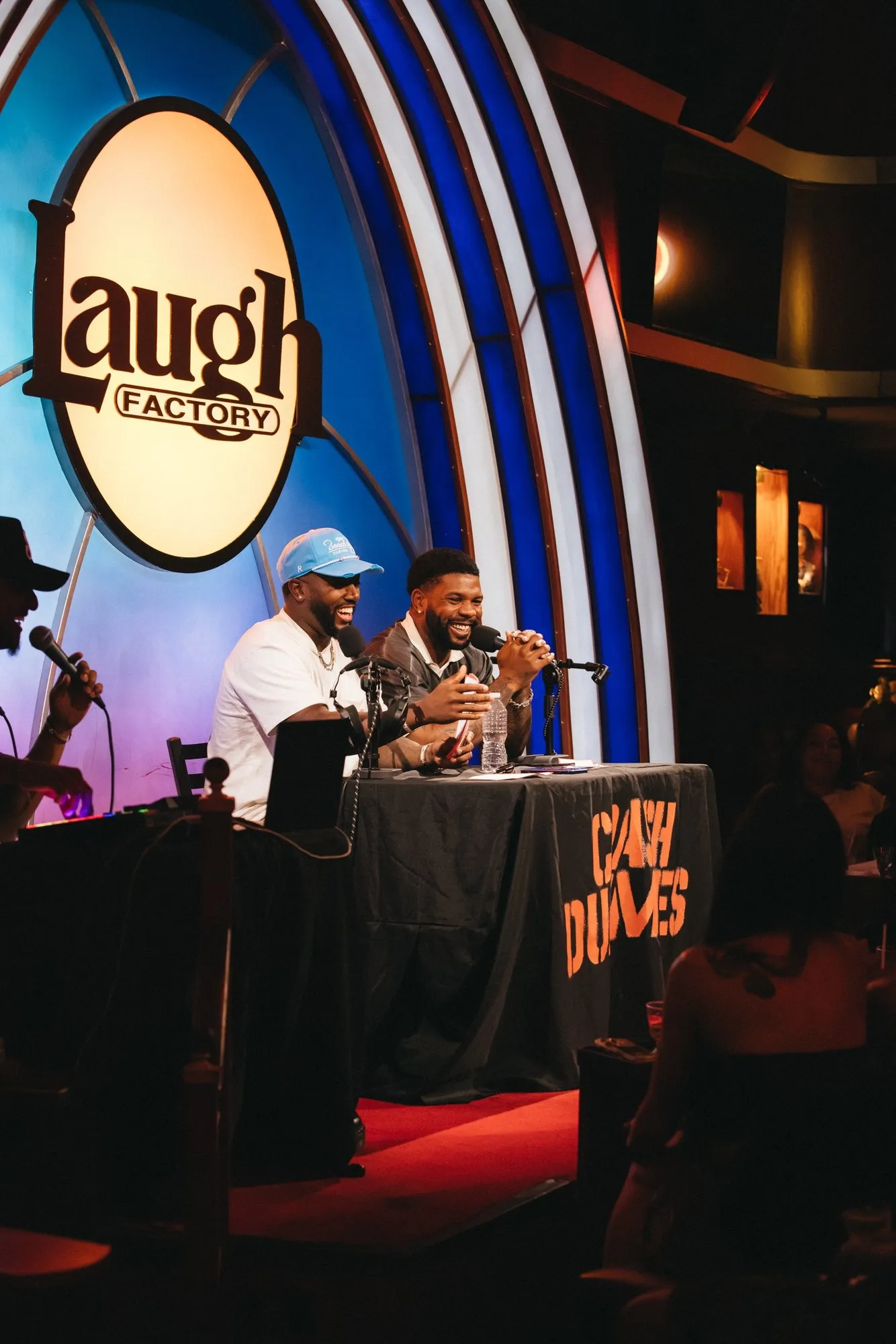 Side view of the hosts at the desk under the Laugh Factory sign